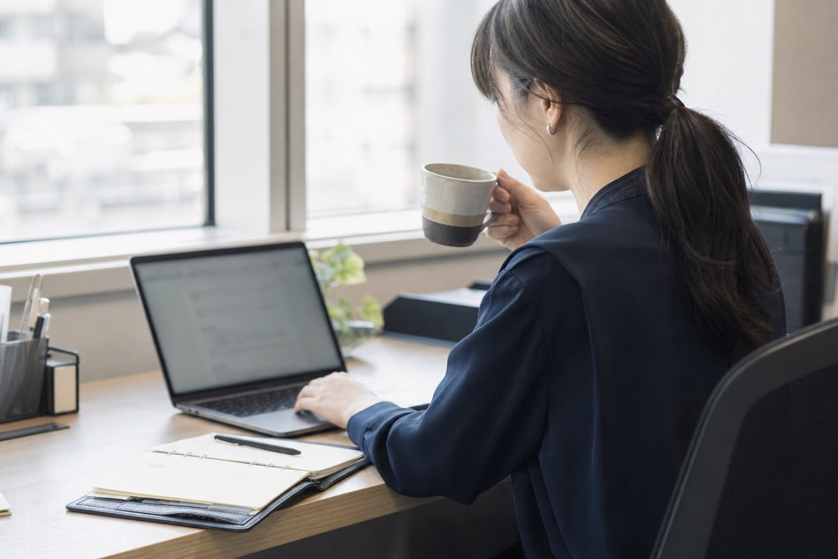 朝のオフィスでノートPCの受信トレイを処理する会社員